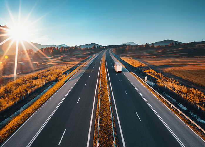 A white truck driving through the highway during sunrise. The other side of the highway is empty.