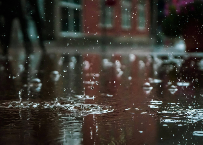 Raindrops fall in a puddle in front of a business building in the distant background